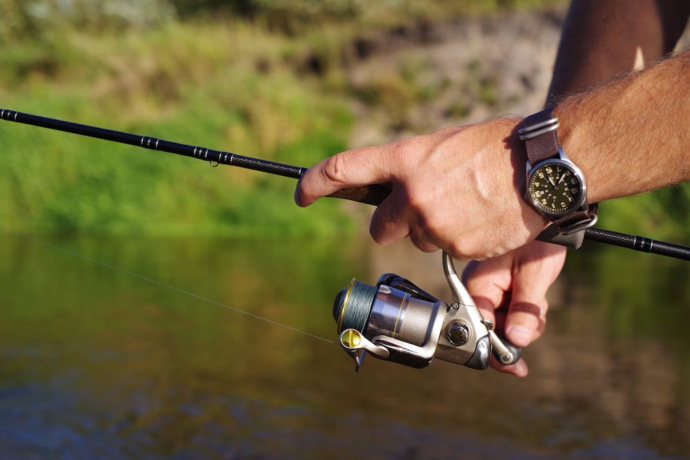 Fishing with a spinning on the river. Man catches fish, a close up of a hand and the spinning reel.