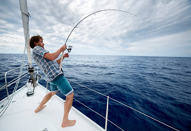Young man fishing in open sea from sail boat